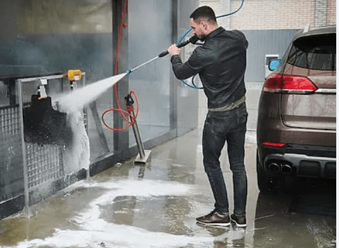 Customer using self-service car wash bay with high-pressure sprayer